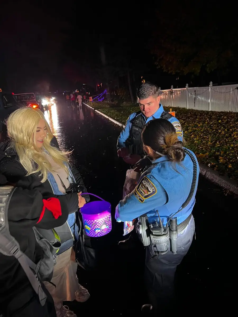 A police officer and volunteer handing out candy at night